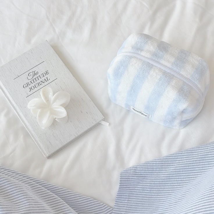 Diário de gratidão e necessaire listrada sobre cama branca